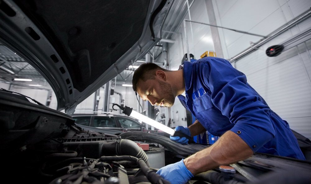 mechanic man with lamp repairing car at workshop PXH46FT